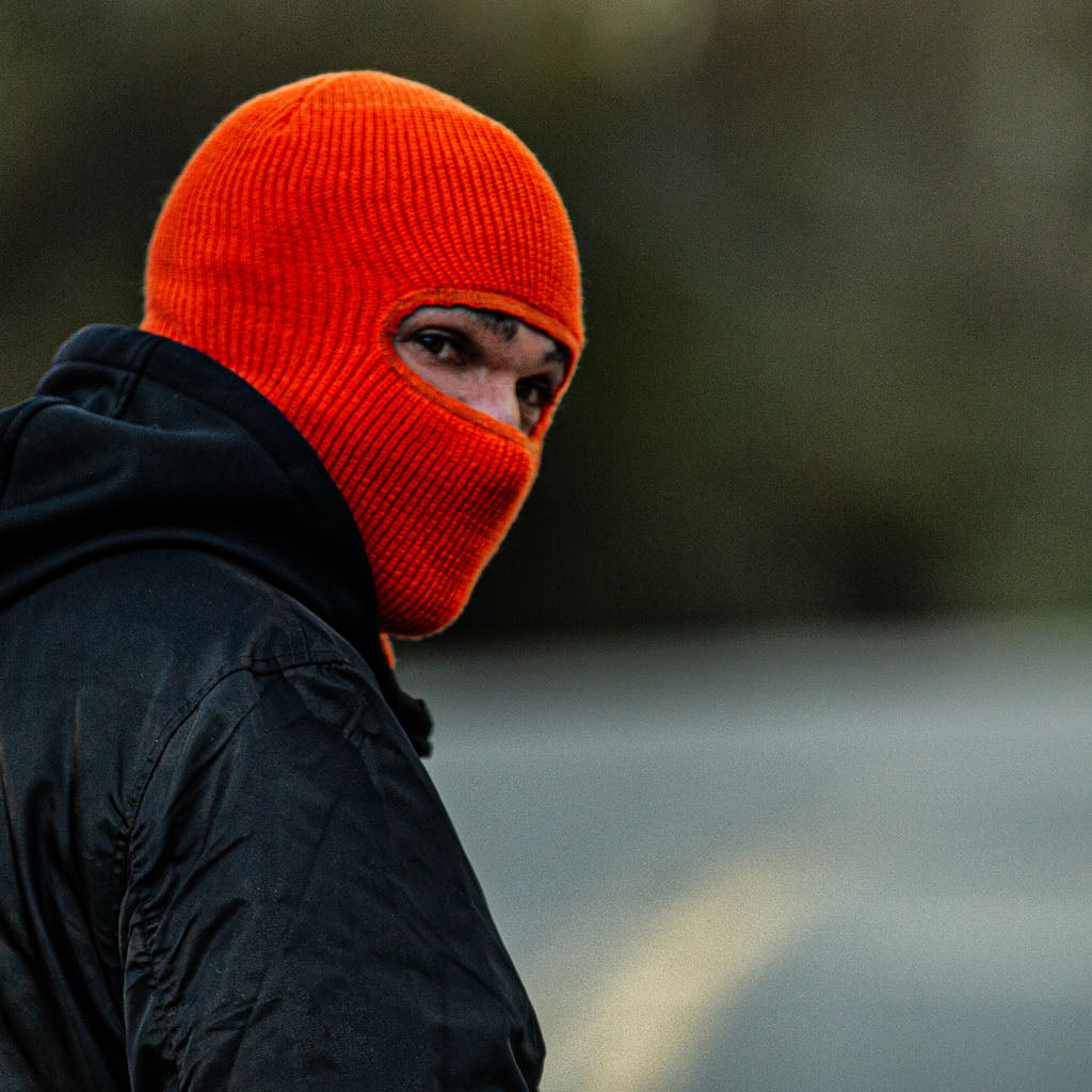 all-groups Blvnk Heist Robber Mask on man looking over his shoulder walking down a forest road.