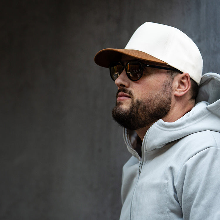 all-groups Blvnk Headwear Vision Vintage Shape Snapback Hat NATURAL BROWN SUEDE on man in hoodie agains a concrete wall.