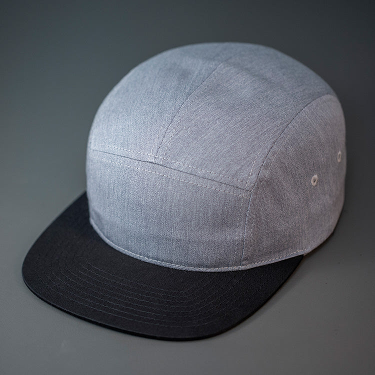 A Heather Grey & Black, Cotton Twill, Blank 5 Panel Camp Hat With a Flat Bill, & Woven Nylon Strapback. Designed by Blvnk Headwear.