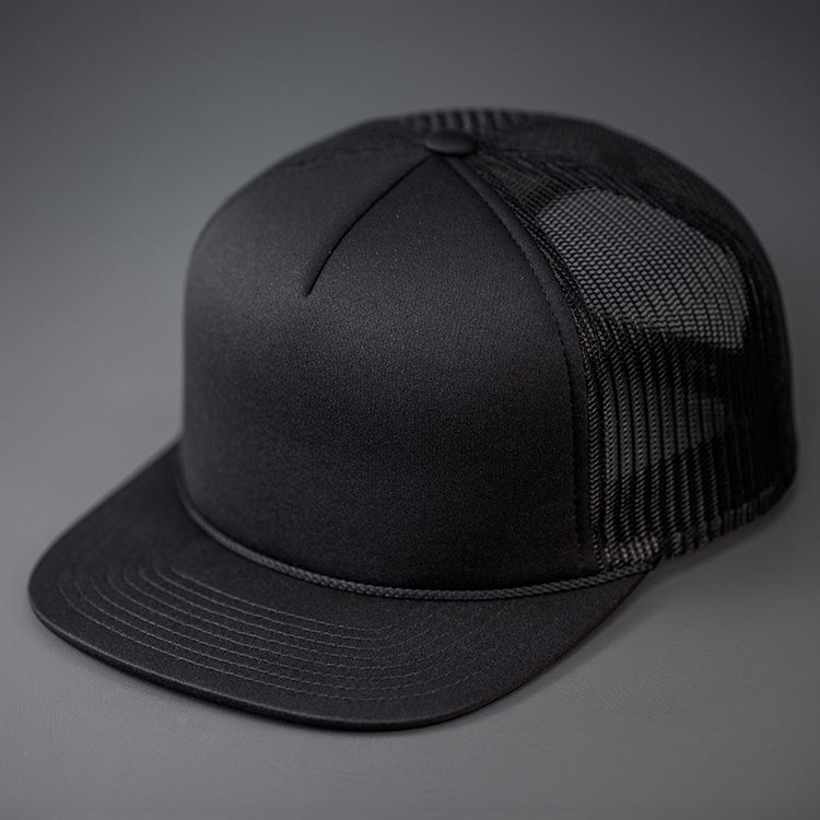 An all Black, Foam Front, Mesh Backed Blank Trucker Hat with a Flat Bill, & Classic Snapback. Designed by Blvnk Headwear.
