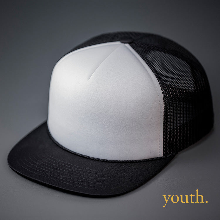 A Youth Sized, White & Black, Foam Front, Mesh Backed Blank Trucker Hat with a Flat Bill, & Classic Snapback. Designed by Blvnk Headwear.