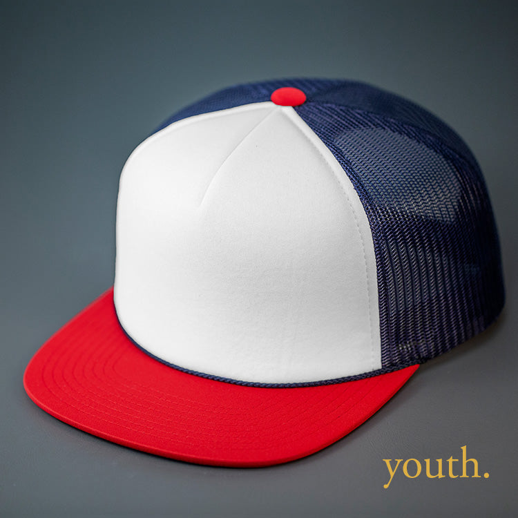 A Youth Sized, White, Navy & Red, Foam Front, Mesh Backed Blank Trucker Hat with a Flat Bill, & Classic Snapback. Designed by Blvnk Headwear.