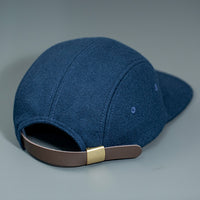 A Navy, Melton Wool, Blank 4 Panel Hat with a Flat Bill, & Vegan Leather Strapback back angle.  Designed by Blvnk Headwear.