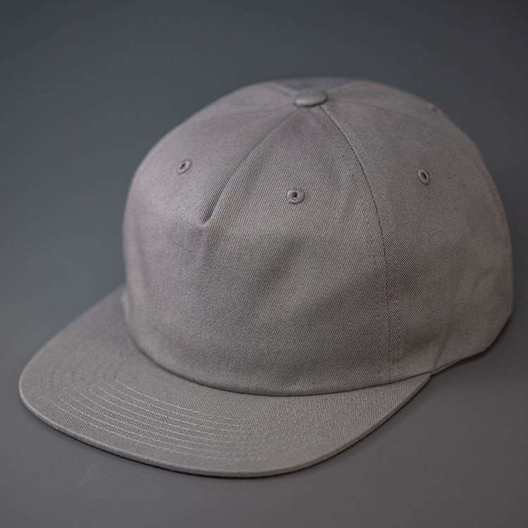 An Light Steel Grey, Unstructured, Premium Cotton, Blank Pinch Front Hat With a Vegan Leather Back Strap & Brass Clasp. Designed By Blvnk Headwear.