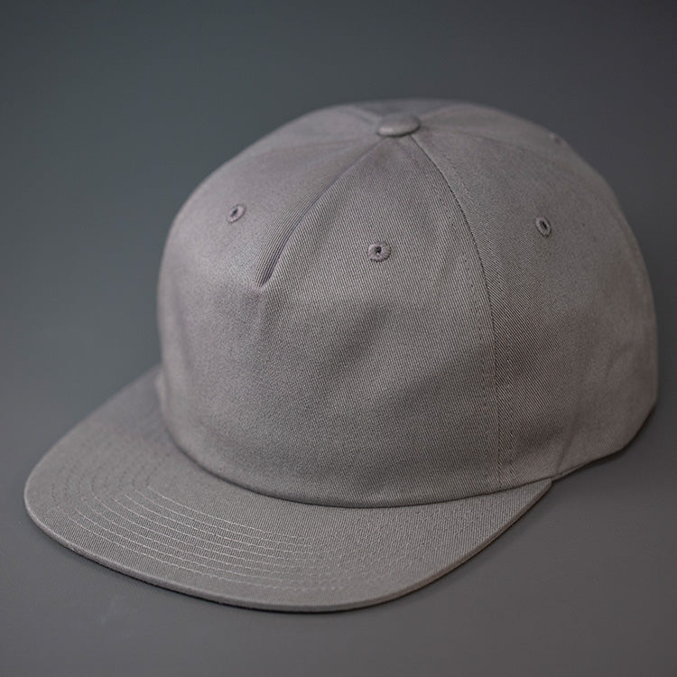 An Light Steel Grey,  Unstructured, Premium Cotton, Blank Pinch Front Hat With a Vegan Leather Back Strap & Brass Clasp.  Designed By Blvnk Headwear.