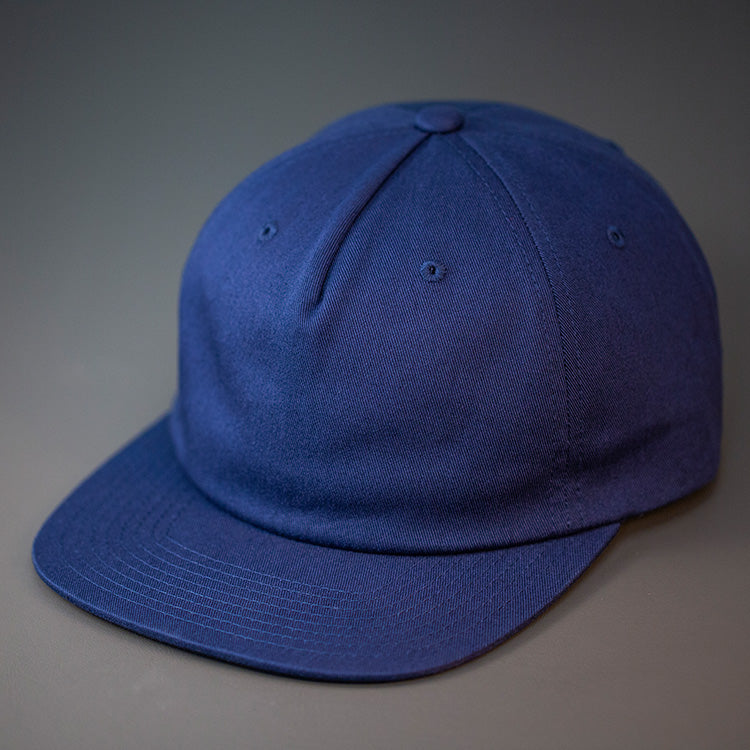 A Navy Blue, Unstructured, Premium Cotton, Blank Pinch Front Hat With a Vegan Leather Back Strap & Brass Clasp. Designed By Blvnk Headwear.