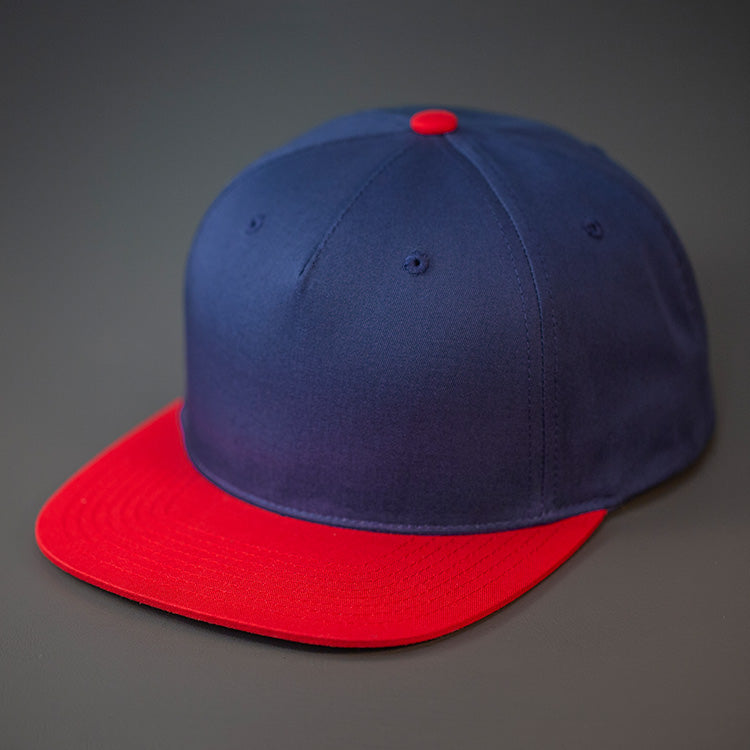 A Navy & Red Colored, Cotton Twill, Pinch Front, Blank Snapback Hat. Designed & Manufactured by Blvnk Headwear.