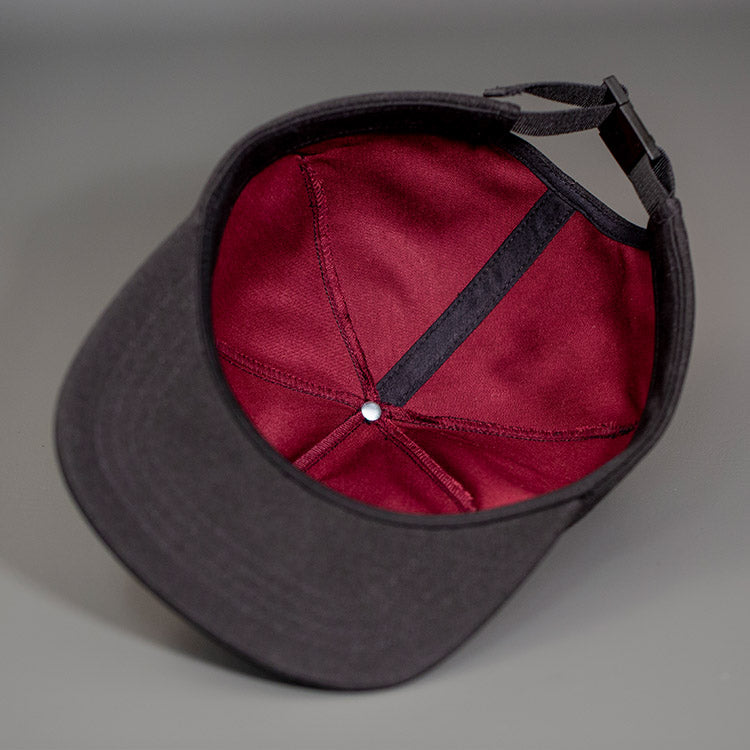 A Maroon Cotton Lining of the Black Chambray, Blank 1 Panel Hat, W/ a Flat Bill & Woven Nylon Strapback.  Designed by Blvnk Headwear.