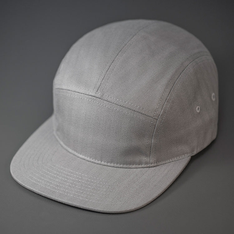 A Grey, Herringbone, Blank 5 Panel Camp Hat With a Flat Bill. Designed by Blvnk Headwear.