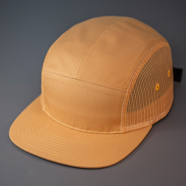 A Biscuit colored, Cotton Twill/Mesh, Blank 5 Panel Camp Trucker Hat With a Flat Bill, & Woven Nylon Strapback. Designed by Blvnk Headwear.