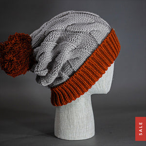 The Northstar Beanie, a heather grey & rust colored, extra long cable knit knit, blank beanie with oversized Pom Pom. Designed by Blvnk Headwear.