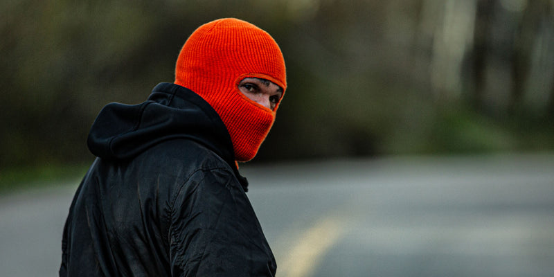 all-groups Blvnk Heist Robber Mask on man looking over his shoulder walking down a forest road.