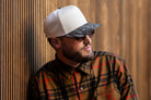all-groups Blvnk Headwear Origin Vintage Shape blank Snapback in Natural and Realtree Original Camo bill on man in a flannel against a wood slat backdrop.