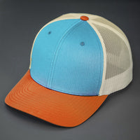 A Columbia Blue, Birch & Dark Orange, Cotton Twill, Mesh Backed, Blank Trucker Hat with a Pre Curved Bill, & Classic Snapback. | Designed by Blvnk Headwear