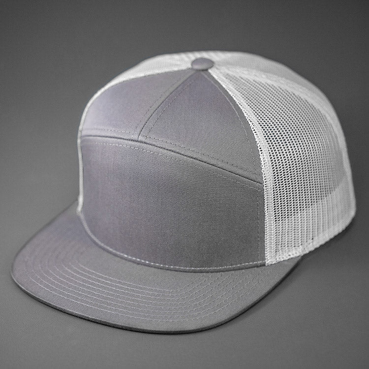 A Heather Grey & White, Cotton Twill, Mesh Backed Blank 7 Panel Trucker Hat with a Flat Bill, & Classic Snapback. Designed by Blvnk Headwear