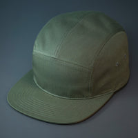 An Army Olive, Cotton Twill, Blank 5 Panel Camp Hat With a Flat Bill, & Woven Nylon Strapback.  Designed by Blvnk Headwear