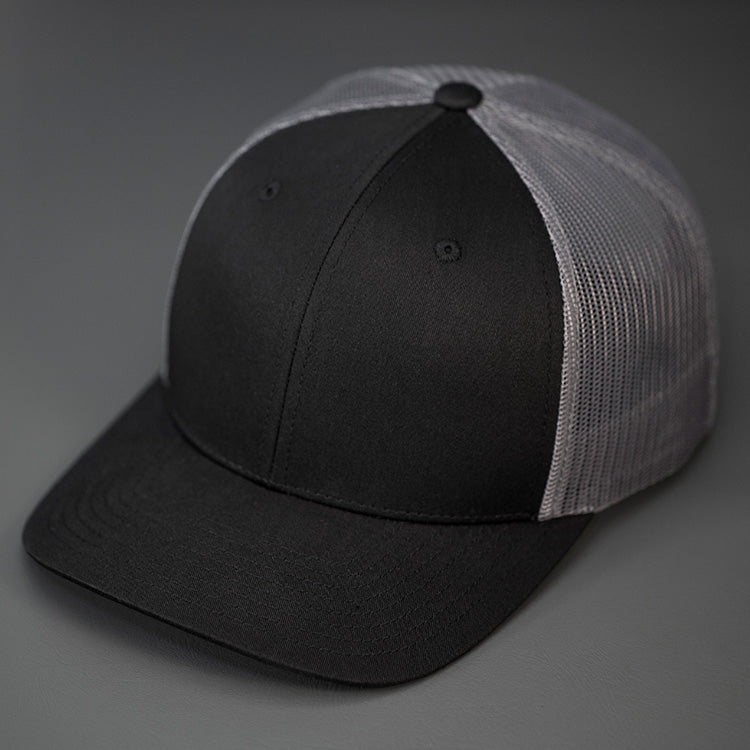 A Black and Charcoal, Cotton Twill, Mesh Backed, Blank Trucker Hat with a Pre Curved Bill, & Classic Snapback.  |  Designed by Blvnk Headwear