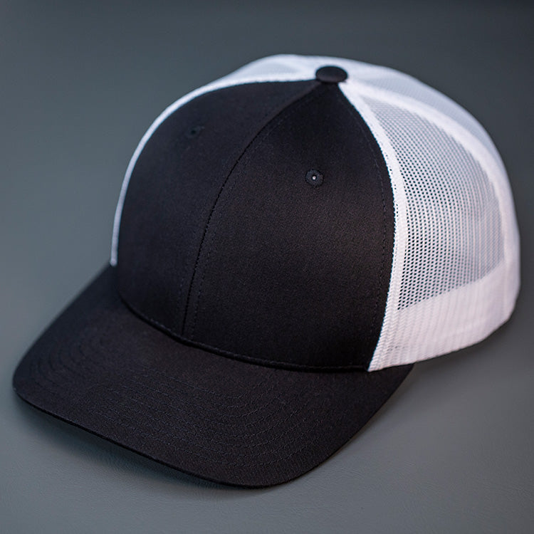 A Black & White, Cotton Twill, Mesh Backed, Blank Trucker Hat with a Pre Curved Bill, & Classic Snapback.  |  Designed by Blvnk Headwear