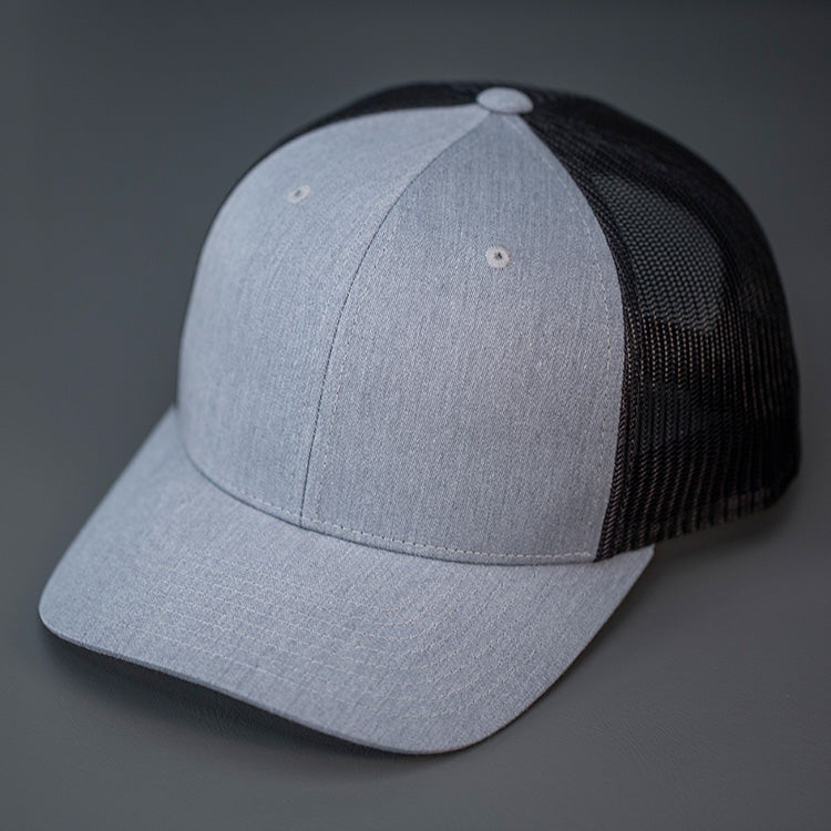 A Heather Grey & Black, Cotton Twill, Mesh Backed, Blank Trucker Hat with a Pre Curved Bill, & Classic Snapback.  |  Designed by Blvnk Headwear