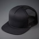 An all Black, Foam Front, Mesh Backed Blank Trucker Hat with a Flat Bill, & Classic Snapback.  Designed by Blvnk Headwear.