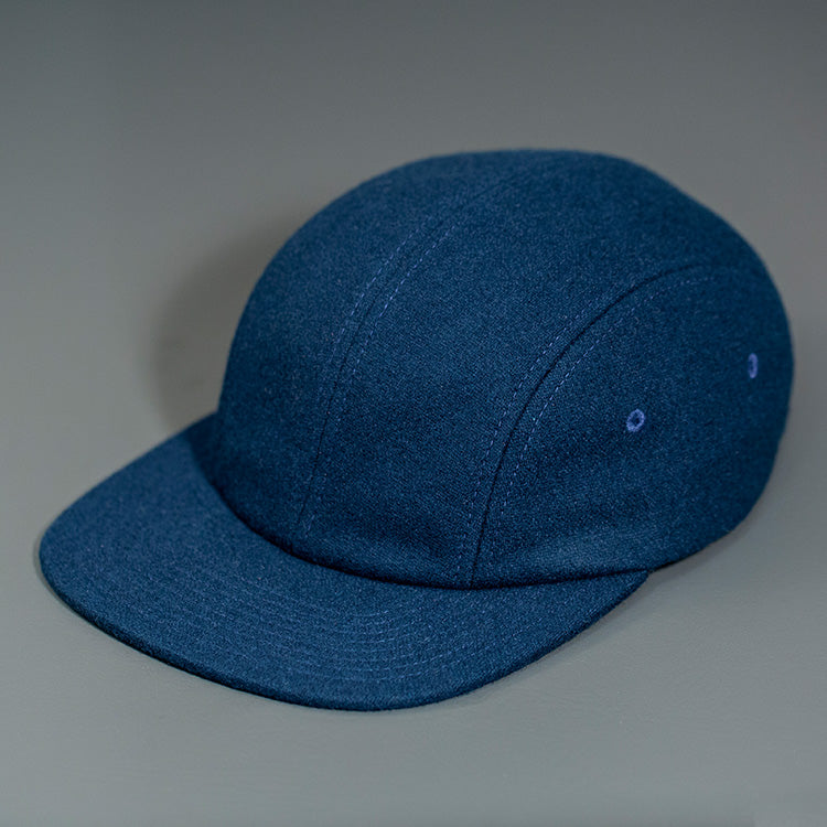 A Navy, Melton Wool, Blank 4 Panel Hat with a Flat Bill, & Vegan Leather Strapback.  Designed by Blvnk Headwear.
