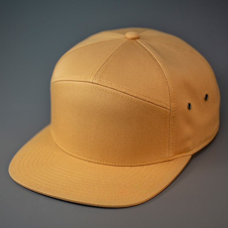 A Biscuit colored, Cotton Twill, Blank 7 Panel Hat with a Flat Bill, Brass Details, & Vegan Leather Strapback.  Designed by Blvnk Headwear