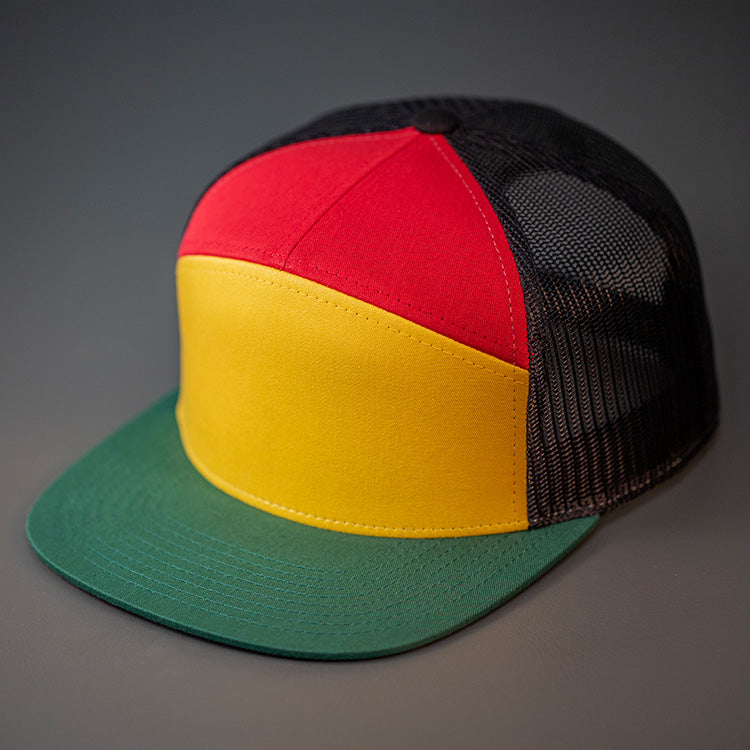 A Rasta Colored, Cotton Twill, Mesh Backed Blank 7 Panel Trucker Hat with a Flat Bill, & Classic Snapback.  Designed by Blvnk Headwear