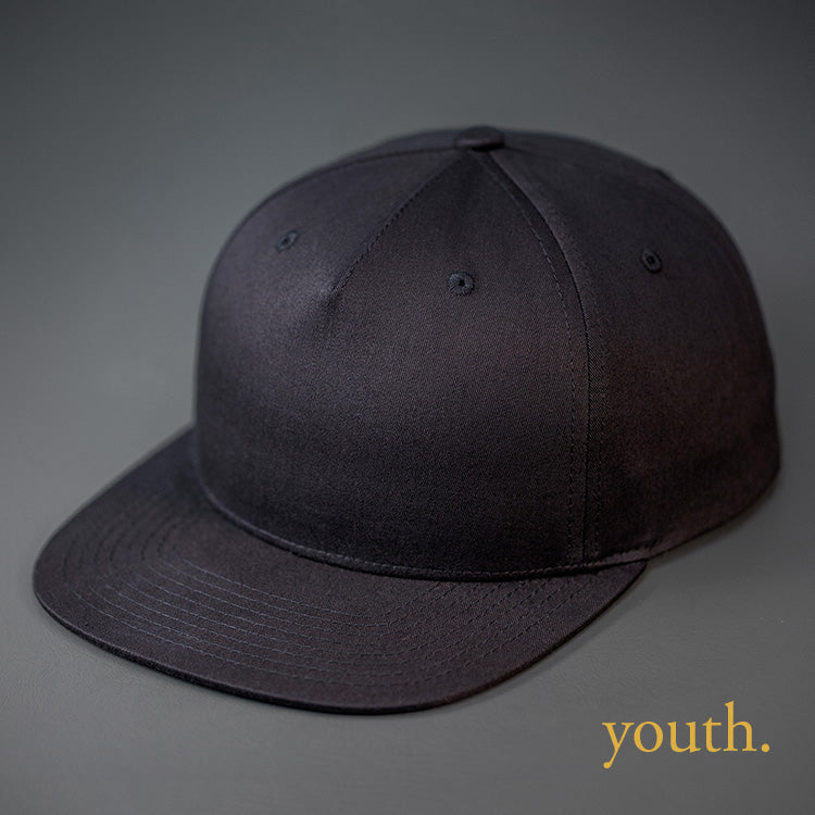 A Youth Sized, Black Colored, Cotton Twill, Pinch Front, Blank Snapback Hat.  Designed & Manufactured by Blvnk Headwear.