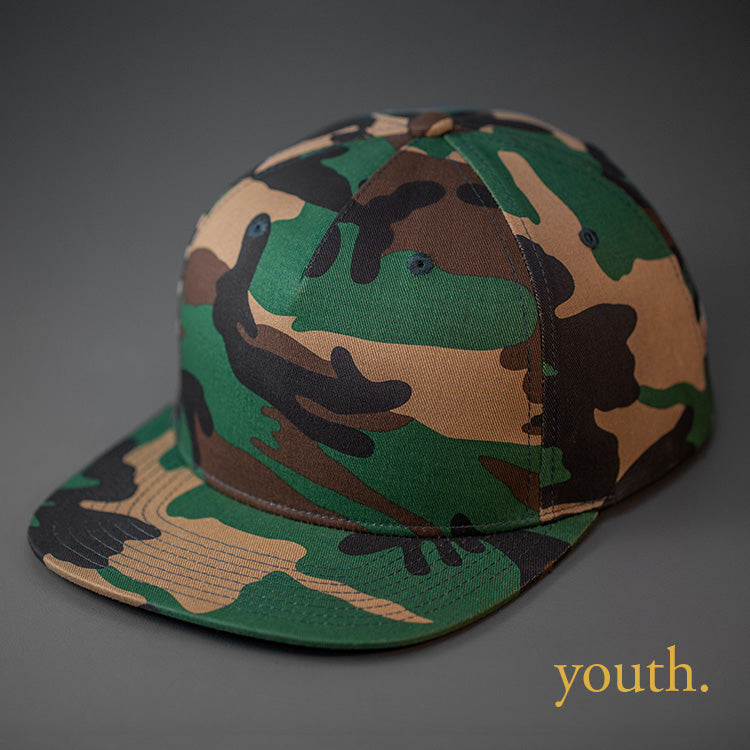 A Youth Sized, Camo Colored, Cotton Twill, Pinch Front, Blank Snapback Hat.  Designed & Manufactured by Blvnk Headwear.