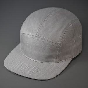 A Grey, Herringbone, Blank 5 Panel Camp Hat With a Flat Bill.  Designed by Blvnk Headwear.