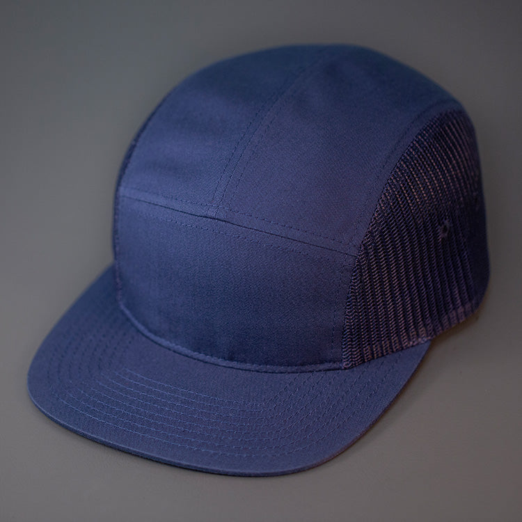 A Navy Blue, Cotton Twill/Mesh, Blank 5 Panel Camp Trucker Hat With a Flat Bill, & Woven Nylon Strapback.  Designed by Blvnk Headwear.